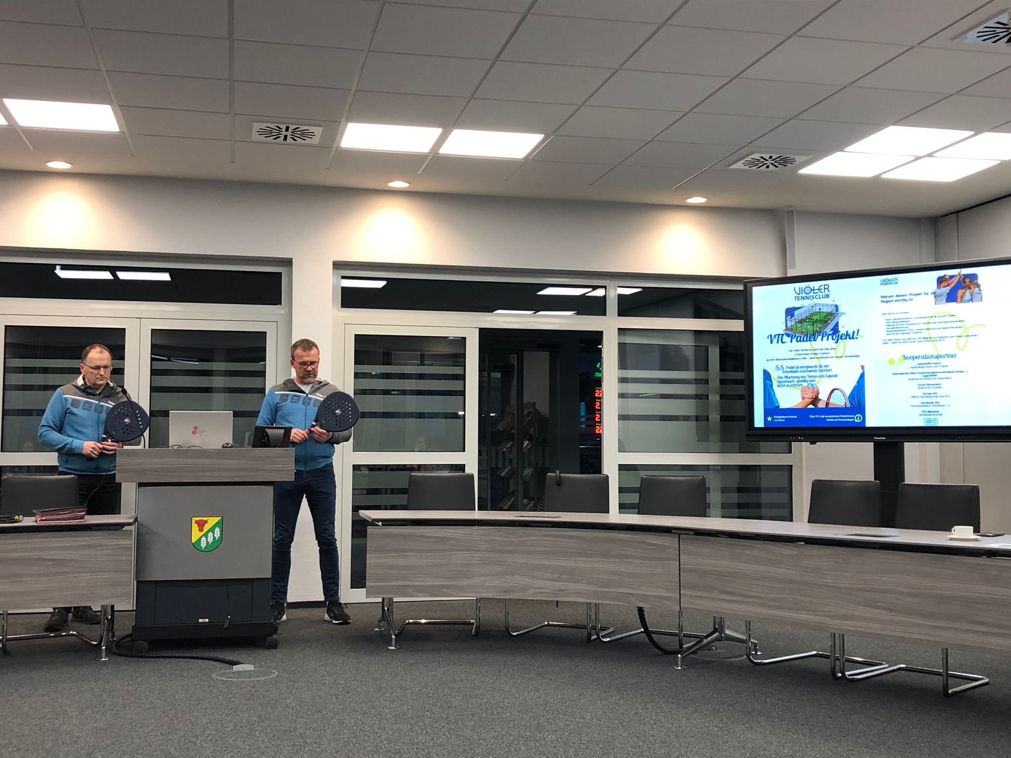 Zwei Personen mit Padel-Tennisschlägern in der Hand präsentieren ihr Projekt auf einer Sitzung